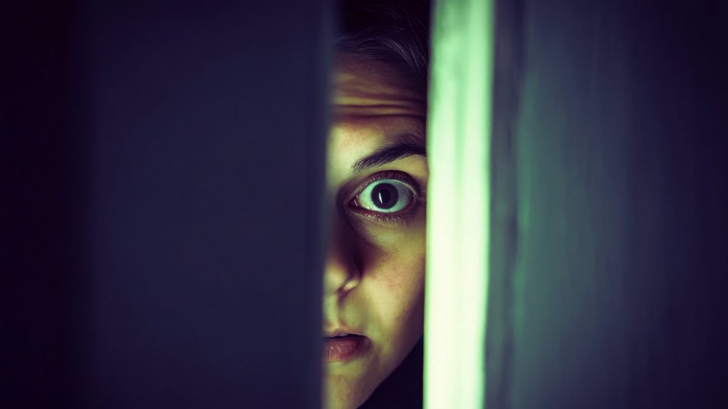 A close-up of a person’s eye peering through a partially opened door.