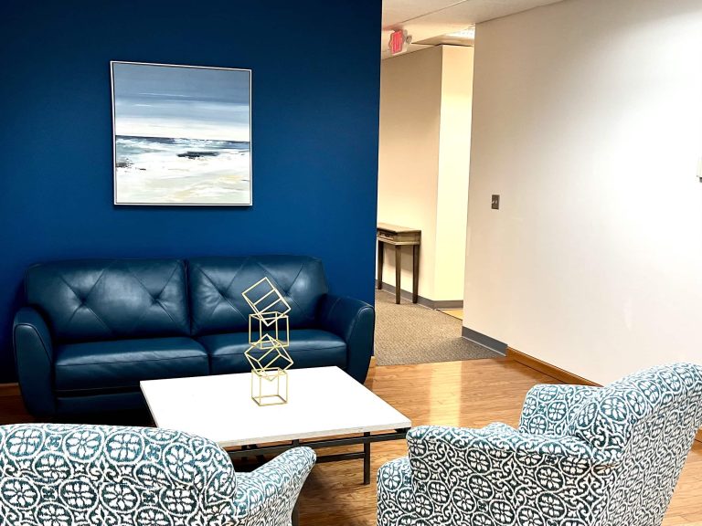 Blueview lounge area with blue sofa, patterned chairs, coffee table, and ocean artwork on a blue wall.
