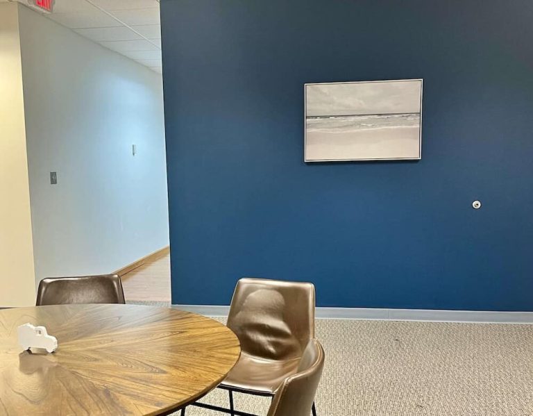 Blueview break area with round table, chairs, and framed beach artwork on a blue wall.