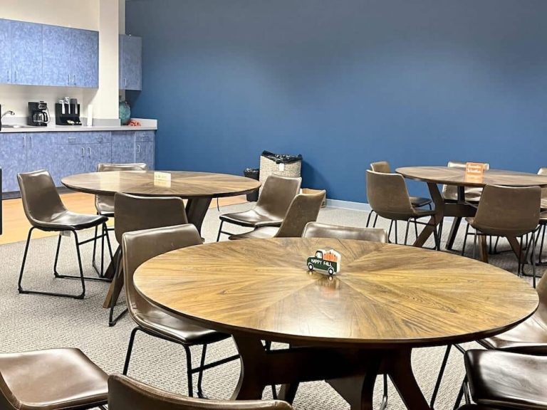 Blueview break room with round tables, chairs, and kitchenette against a blue wall.