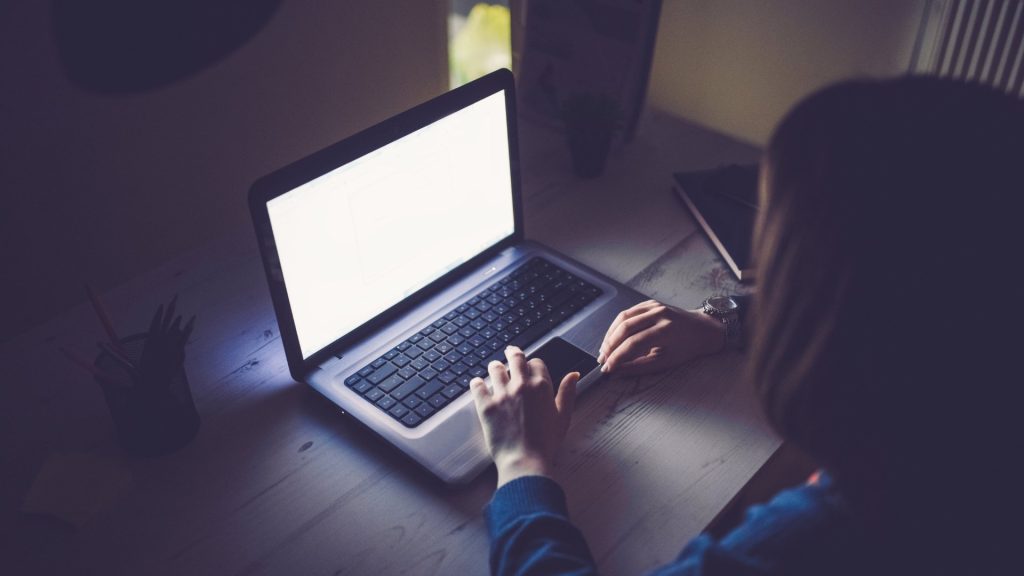 A person working alone on a laptop late at night in a dark room.