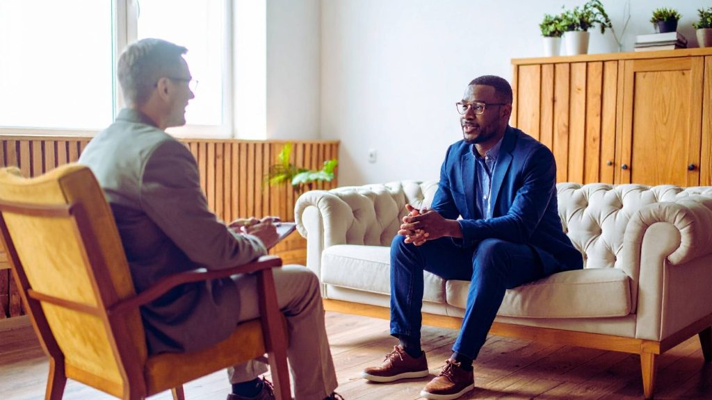 Virtual IOP vs. In-Person IOP: What’s Right for You? 2 Person meeting with a therapist in a calm, professional setting, representing in-person intensive outpatient addiction treatment.